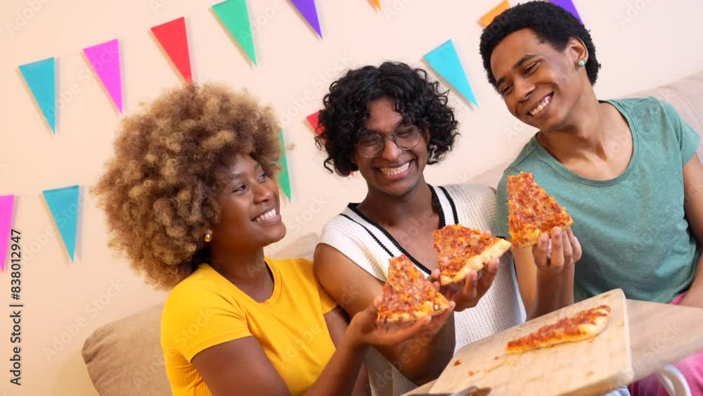 Multi-ethnic friends showing a slice of pizza smiling at camera sitting together on the sofa dutin Multi-ethnic friends showing a slice of pizza smiling at camera sitting together on the sofa dutin