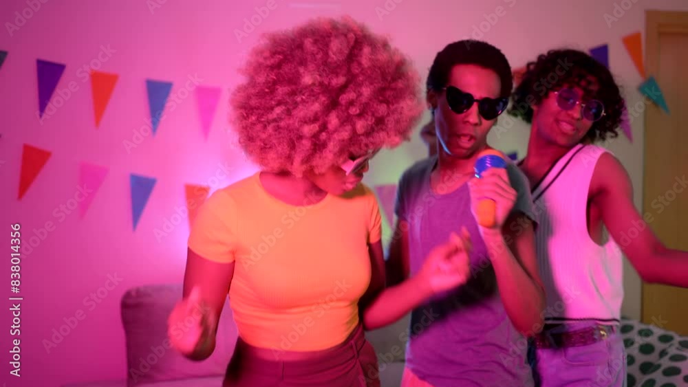 Multi-ethnic friends singing karaoke at home at night with blue neon light illuminating the living room