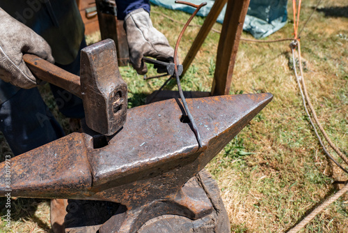 Artesão a trabalhar na bigorna com o martelo a aguçar um pequeno ferro de metal que acabou de sair da forja 