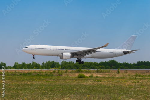 A large white passenger airliner landing on a sunny summer day against the backdrop of a green forest and a cloudless blue sky. Side view.
