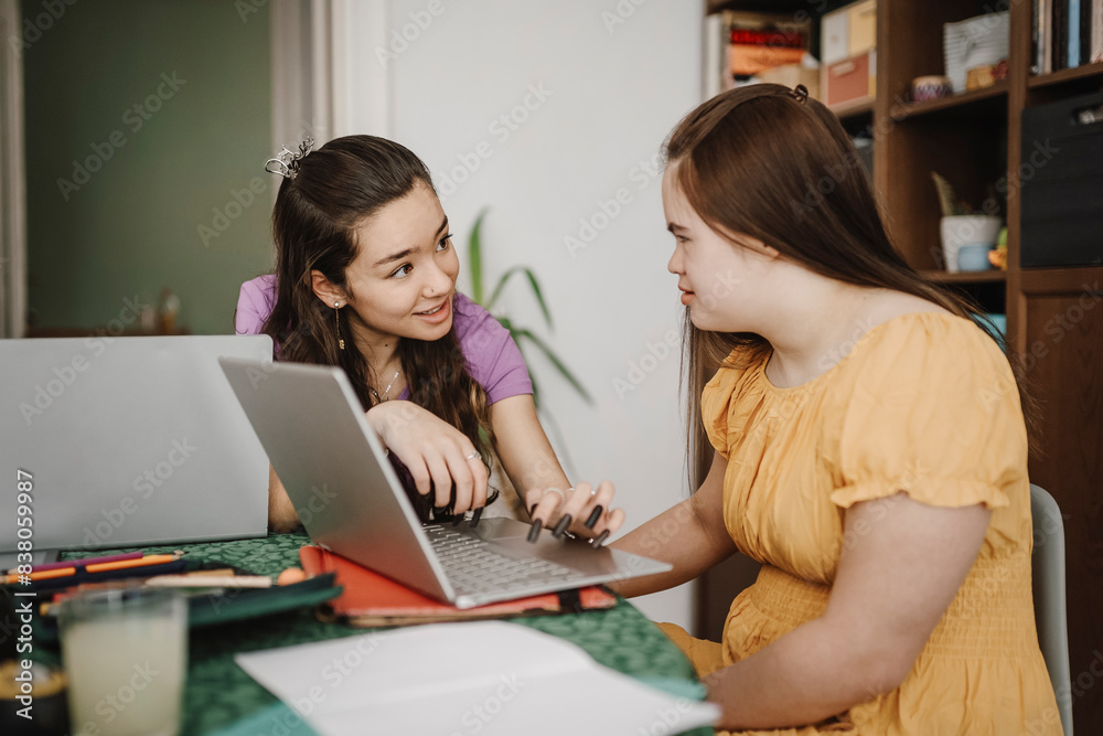 Woman homeschooling disabled sister while sitting with laptop on table at home Woman homeschooling disabled sister while sitting with laptop on table at home