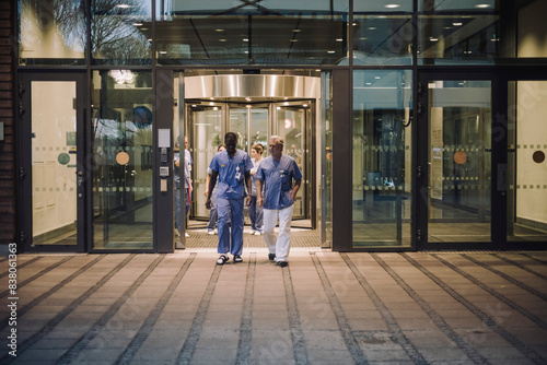 Multiracial male doctors in scrubs leaving hospital at night