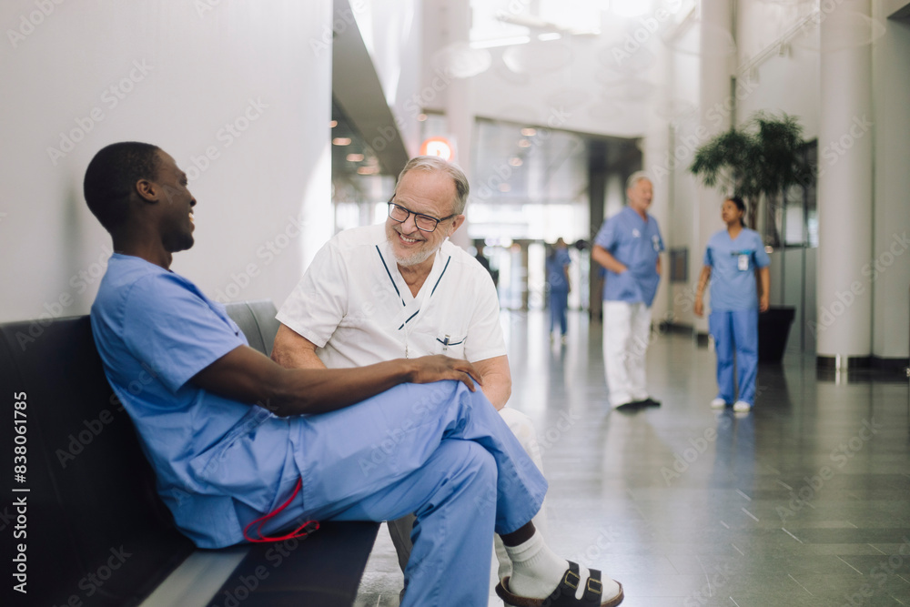 Happy senior doctor discussing with colleague while sitting in corridor of hospital Happy senior doctor discussing with colleague while sitting in corridor of hospital