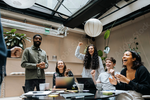 Multiracial male and female entrepreneurs cheering during team meeting at office photo