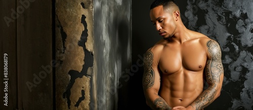 a dark-skinned man of athletic build with a bare torso in tattoos poses