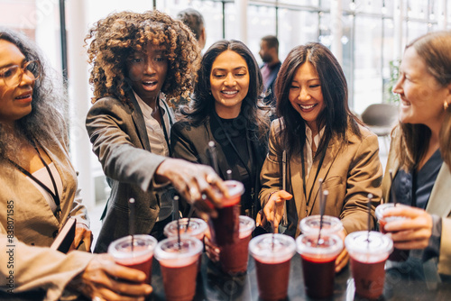 Smiling female entrepreneurs picking up drinks from counter during break at convention center photo