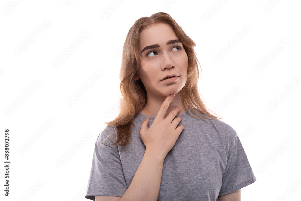 A blonde teenage girl of European appearance in a gray T-shirt is puzzled by solving a problem against a background of copy space A blonde teenage girl of European appearance in a gray T-shirt is puzzled by solving a problem against a background of copy space
