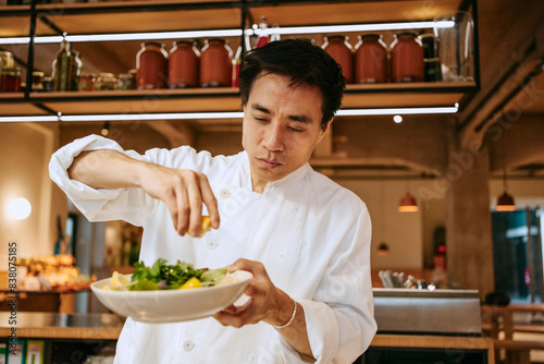 Close-up of male chef squeezing lemon juice on salad at commercial kitchen photo