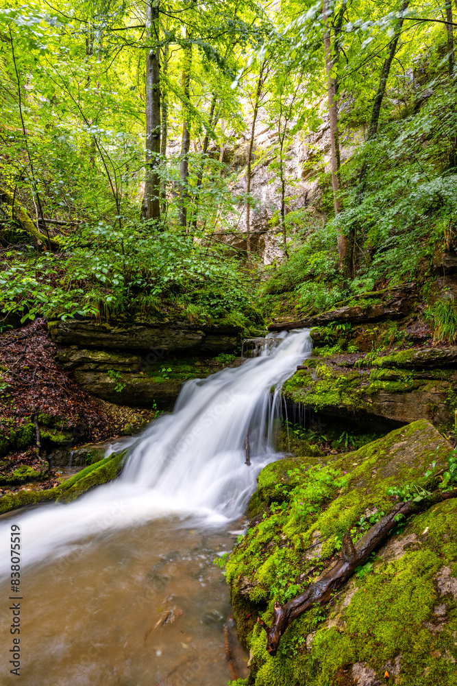 Waterfall near the exit of the “Falkensteiner Höhle” (Falkenstein cave) near Bad Urach (Germany). Karst creek with high level in May from an underground river under “Schäbische Alb” plateau. Waterfall near the exit of the “Falkensteiner Höhle” (Falkenstein cave) near Bad Urach (Germany). Karst creek with high level in May from an underground river under “Schäbische Alb” plateau.