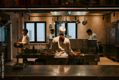 Rear view of female chef standing with colleagues at commercial kitchen photo