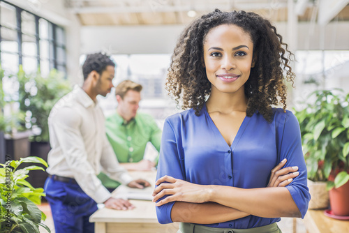 Mujer negra de brazos cruzados y camisa azul. Chica de negocios sobre fondo con gente hablando. Reunón de trabajo.