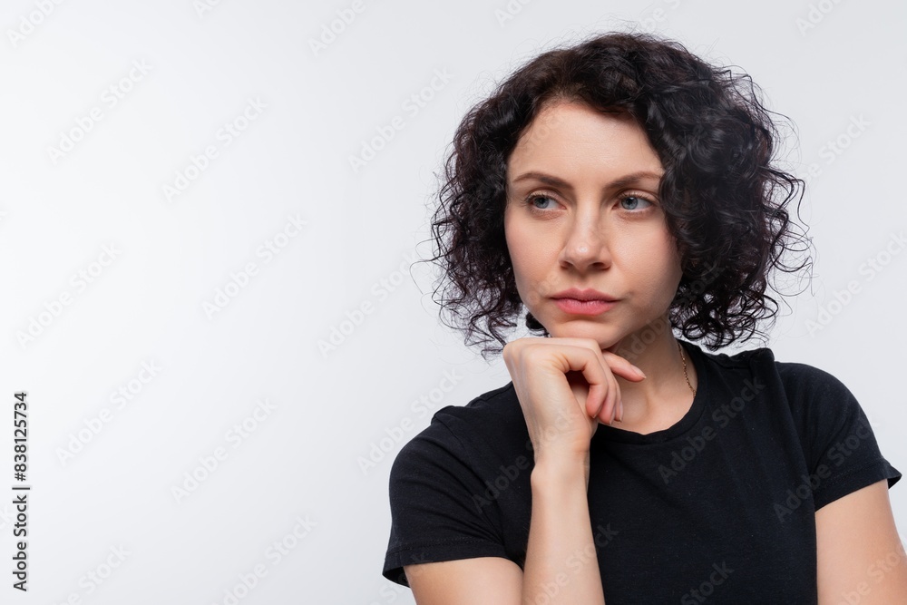 Caucasian woman with black curls looks slyly on a white background with copy space Caucasian woman with black curls looks slyly on a white background with copy space