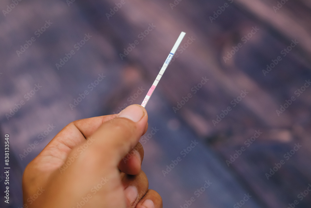Woman hand holding positive pregnancy test strips on wood background Woman hand holding positive pregnancy test strips on wood background