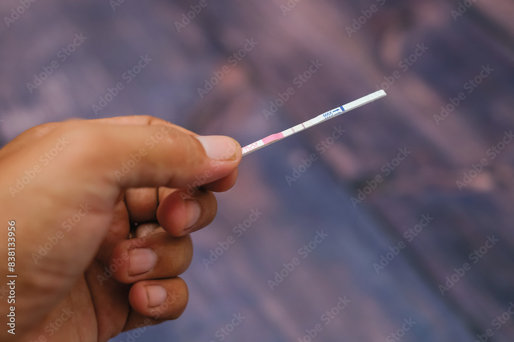 Woman hand holding positive pregnancy test strips on wood background Woman hand holding positive pregnancy test strips on wood background