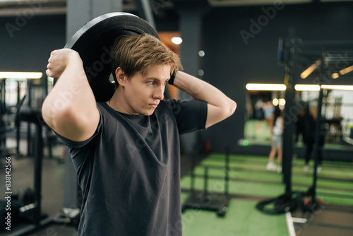 Obraz na plátně Dedicated beginner sportsman in activewear holding and rotating weight disc plate overhead during sport workout training in modern gym