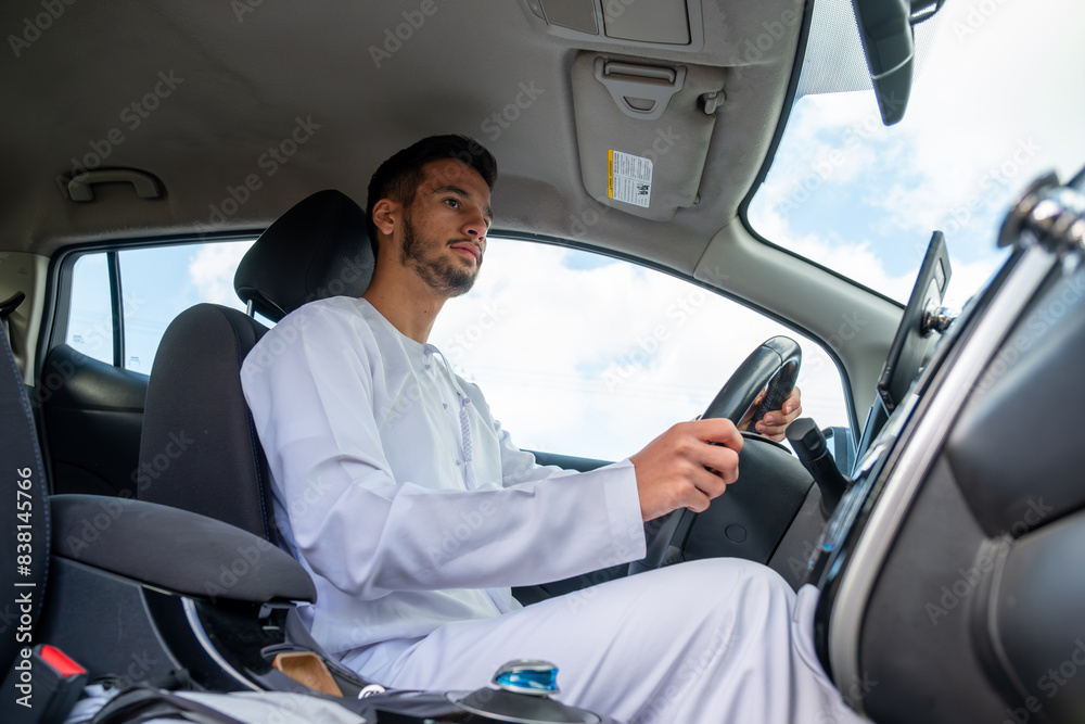 A cheerful young man with a beard, wearing a traditional Middle-Eastern outfit, smiles confidently while seated in his car. He appears to be enjoying a drive through a scenic countryside A cheerful young man with a beard, wearing a traditional Middle-Eastern outfit, smiles confidently while seated in his car. He appears to be enjoying a drive through a scenic countryside