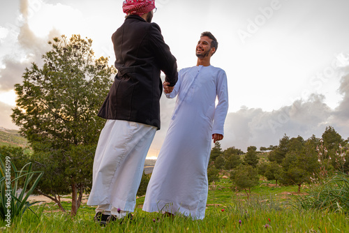 Two Arabic friends shaking hands in nature, having a wonderful time together during springtime in the wild, looking forward to working together in the future