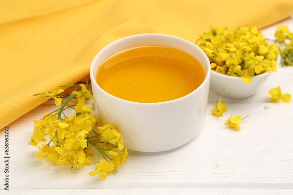 Rapeseed oil in bowl and beautiful yellow flowers on white wooden table Rapeseed oil in bowl and beautiful yellow flowers on white wooden table
