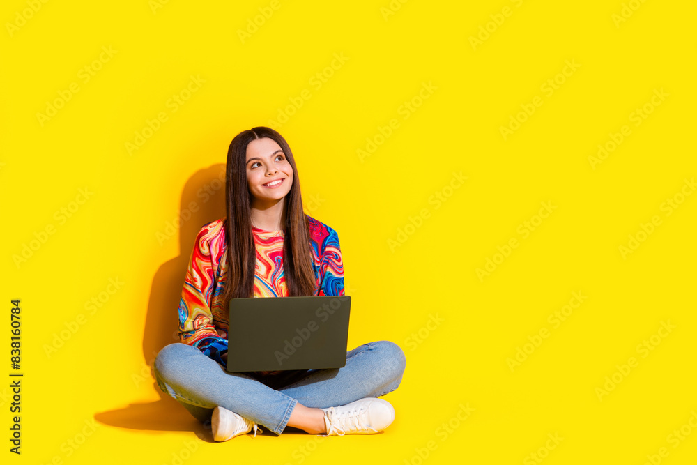 Naklejka premium Full size photo of pretty young girl look empty space netbook wear trendy colorful outfit isolated on yellow color background