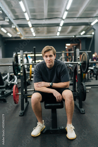 Full length vertical portrait of sportsman having accident injury and hurt at arms while workout with barbell weight training at gym. Athletic man suffering from muscle injury exercising at sport club