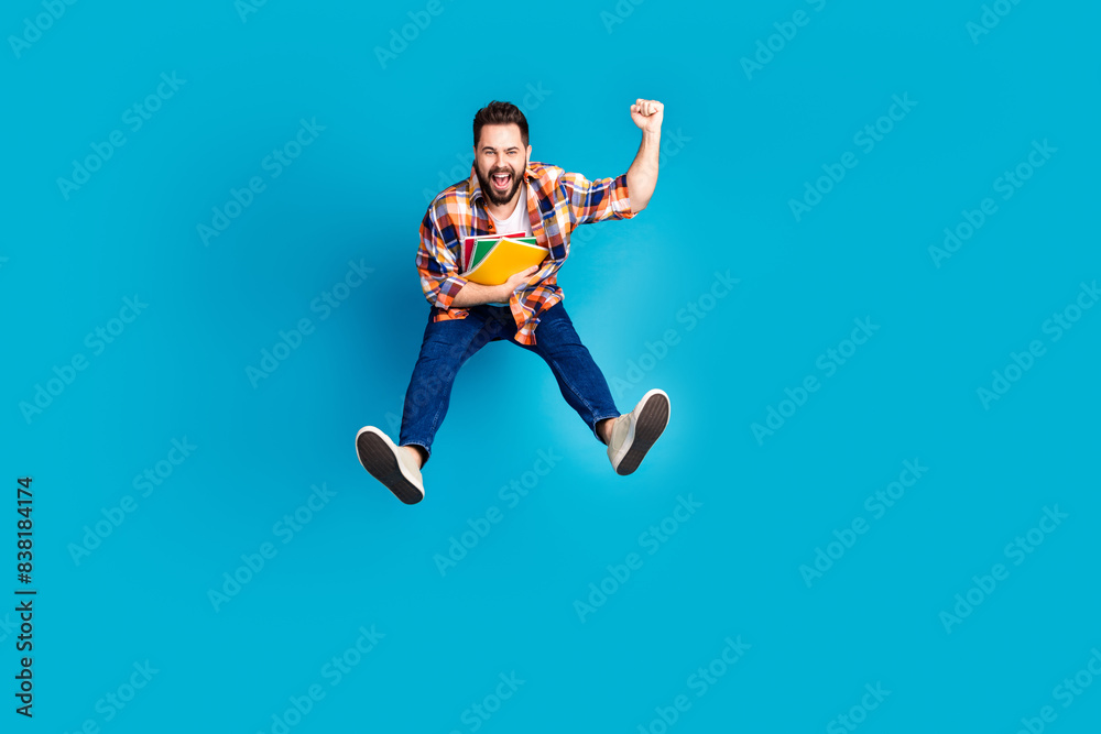 Full length portrait of nice young man jump raise fist wear shirt isolated on blue color background Full length portrait of nice young man jump raise fist wear shirt isolated on blue color background