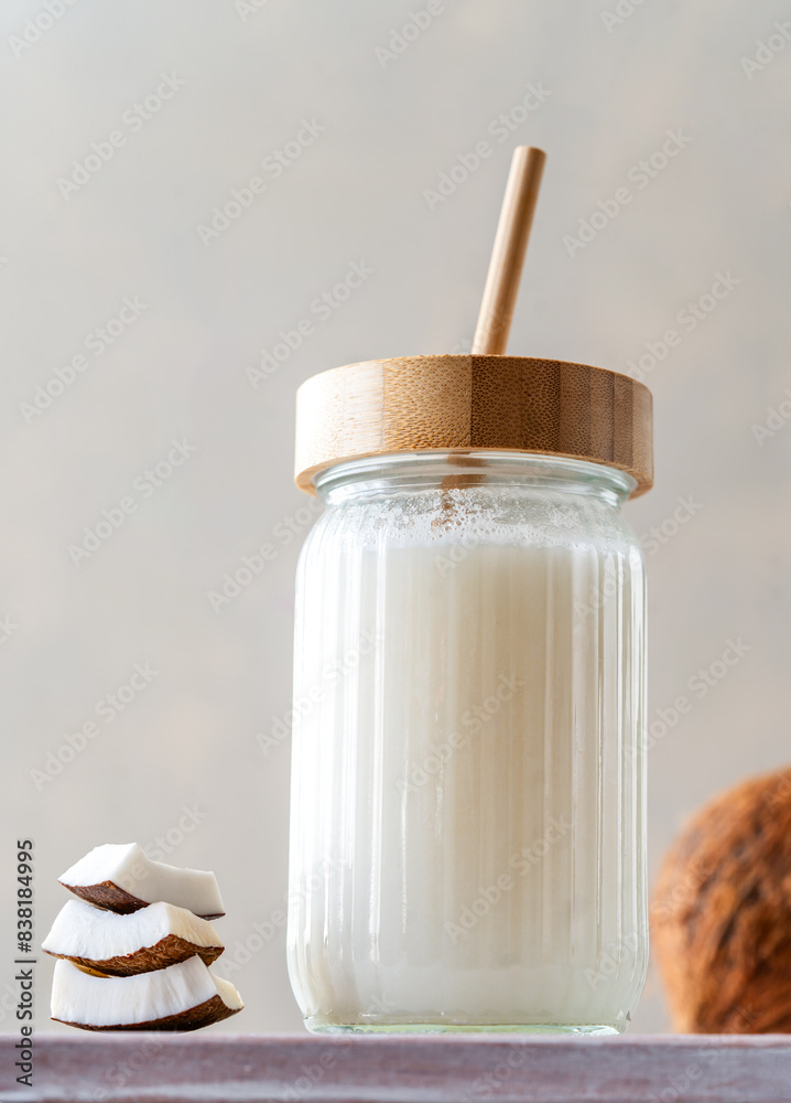 A jar of fresh coconut milk with a bamboo straw, accompanied by stacked coconut slices and a whole coconut on a textured surface.