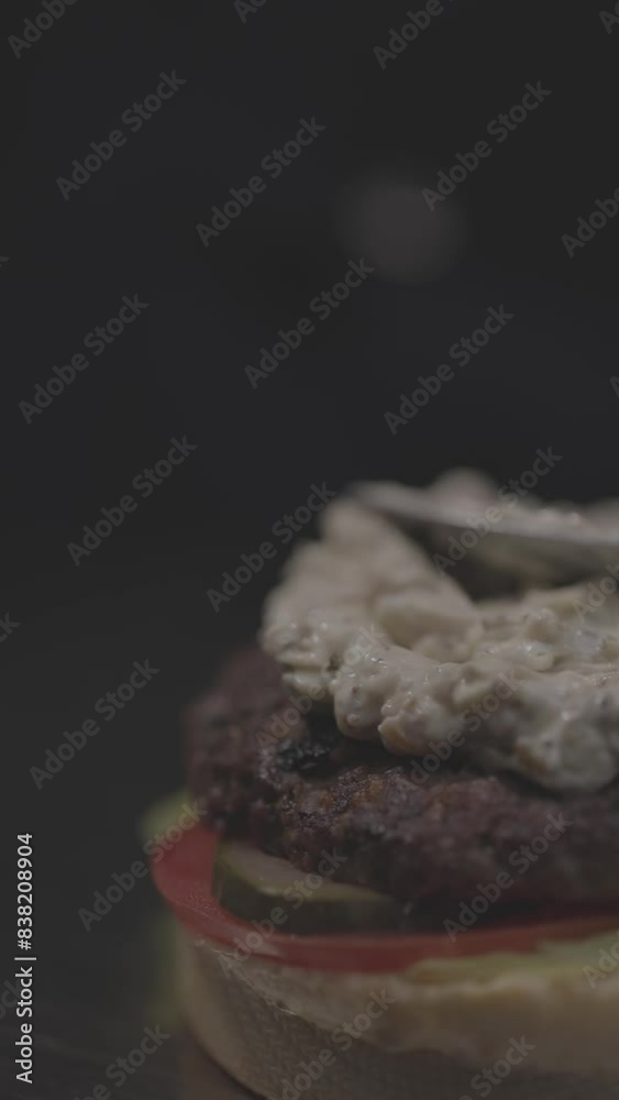 Vertical slow-motion of spoon spreading the sauce in a burger sandwich against dark background Vertical slow-motion of spoon spreading the sauce in a burger sandwich against dark background