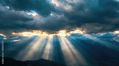 Majestic scene of sun rays filtering through a dark, overcast sky, casting a heavenly glow over a mountain range