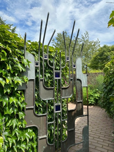 Appeltern, Netherlands, July 11, 2023: Appeltern adventure garden. Decorative wrought iron gate framed by a cascade of vine leaves photo