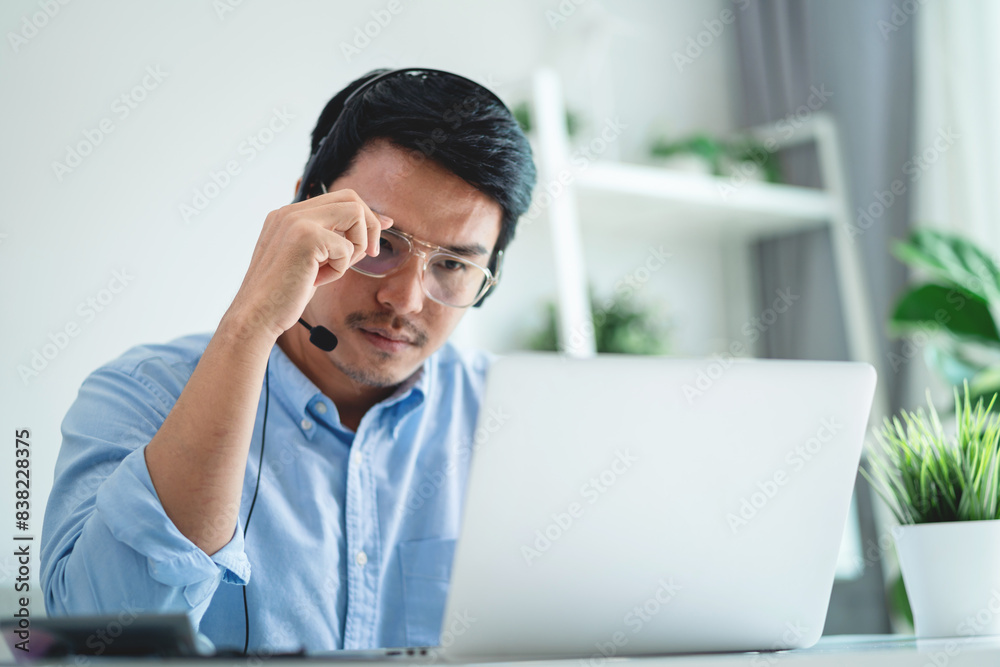 Asian man using headset and computer in modern office Businessman tired from long work, hard work. Asian man using headset and computer in modern office Businessman tired from long work, hard work.