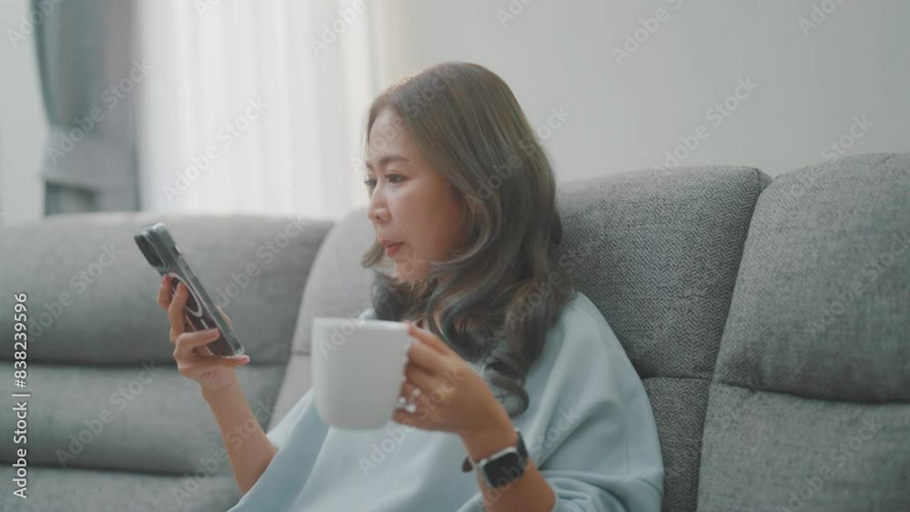 Women are playing with their mobile phones on the sofa and on the dining table and drinking coffee at the same time.