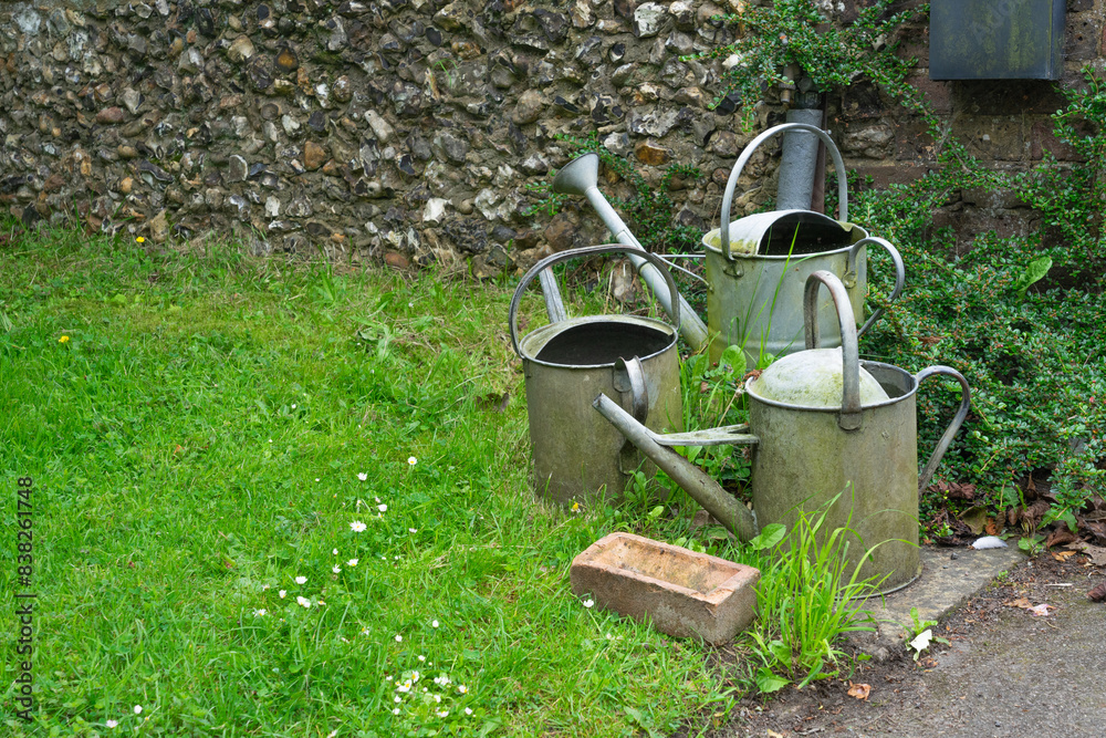 Three watering cans in a garden next to an old wall Three watering cans in a garden next to an old wall