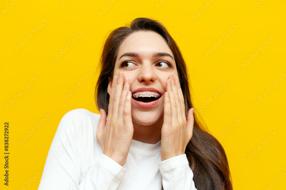 modest woman with braces smiling jokes and mocks covering her smile with her hands on a yellow isolated background, excited girl is shy smiling and surprised in amazement modest woman with braces smiling jokes and mocks covering her smile with her hands on a yellow isolated background, excited girl is shy smiling and surprised in amazement