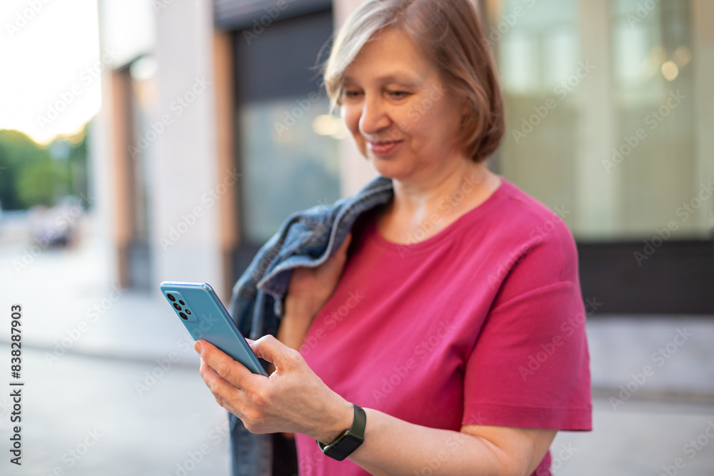 Beautiful smiling mature woman holding smart phone in her hand  on the urban street. 