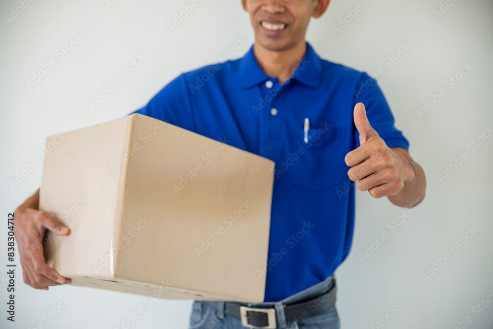Delivery man holding Parcel Box Package to deliver and giving thumb up. Courier hand carries the shipment Service. Delivery Concept. Delivery man holding Parcel Box Package to deliver and giving thumb up. Courier hand carries the shipment Service. Delivery Concept.