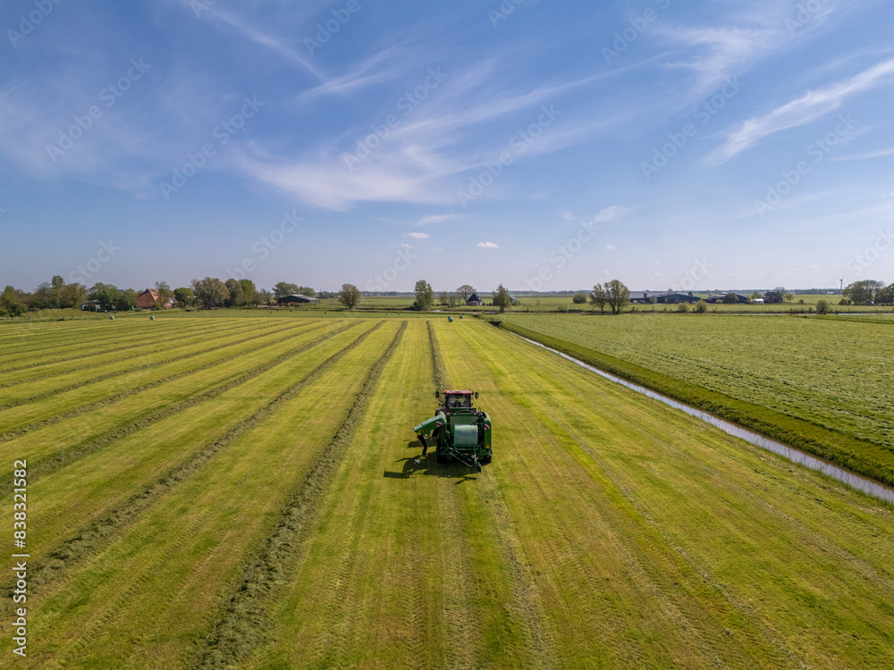 Aerial View: Tractor Gathering Rows of Grass into Piles on Farmland Aerial View: Tractor Gathering Rows of Grass into Piles on Farmland