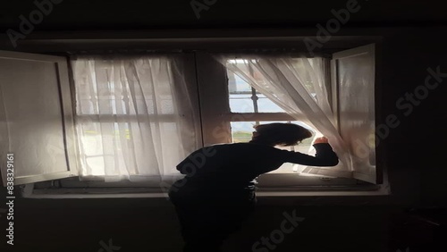 Mujer corriendo las cortinas de una casa colonial en el interior del pais filmado desde el celular photo