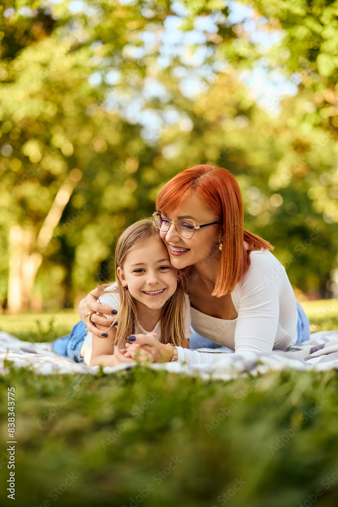 Beautiful mother and daughter lying on a blanket in a hug, smiling and enjoying the sunny day at the park. Beautiful mother and daughter lying on a blanket in a hug, smiling and enjoying the sunny day at the park.
