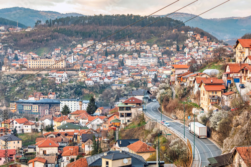 At sunset, Sarajevo's cityscape unfolds, with winding roads weaving through colorful neighborhoods against the backdrop of majestic mountains.