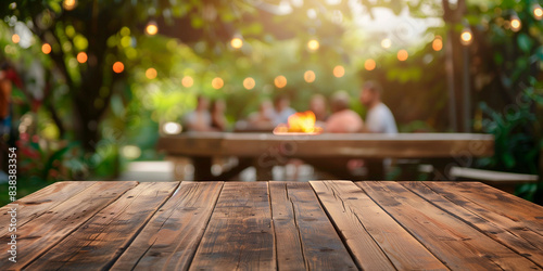 Empty wooden table and blurred view of people having BBQ barbecue with modern grill outdoors
