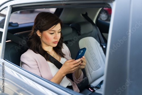Businesswoman checks her smartphone while sitting in the backseat of a modern vehicle, commuting to work © AntonioDiaz