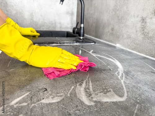 woman wear rubber gloves with a sponge and foam wipes down a kitchen countertop