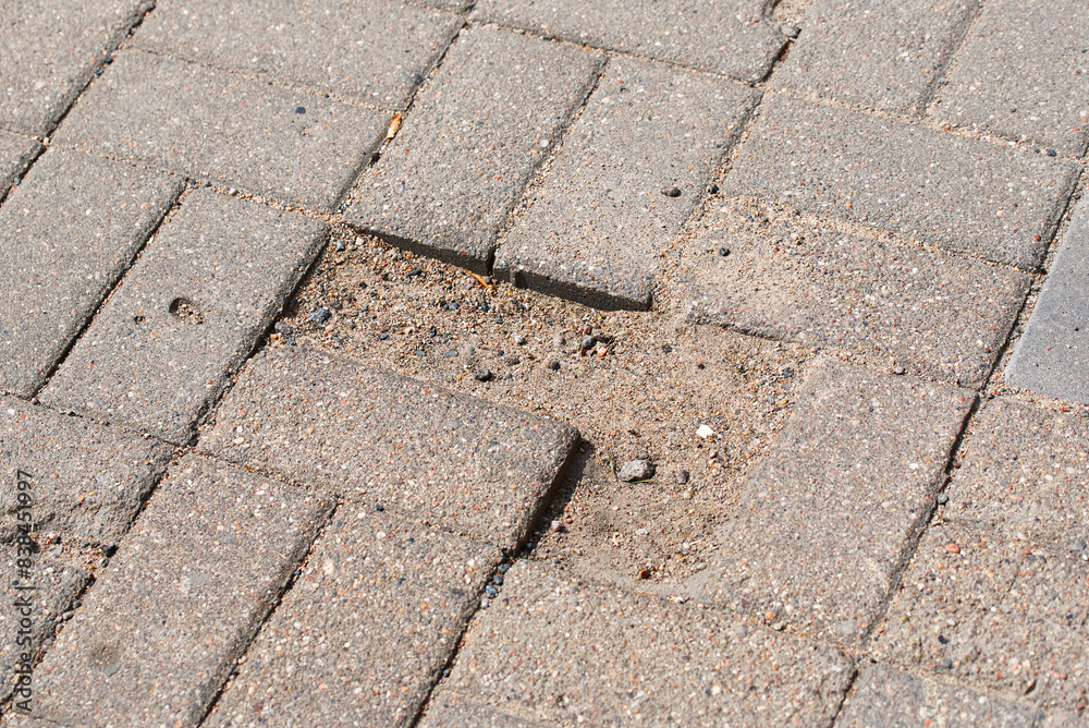 Sidewalk with pothole. Defects on paving slabs, improperly laid paving stones. Inferior or insufficient bedding sand might cause pavers to move and break. Paving failure, improperly laid paving stones