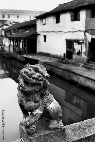 A stone lion statue positioned on a bridge, overlooking a serene canal in an old town photo