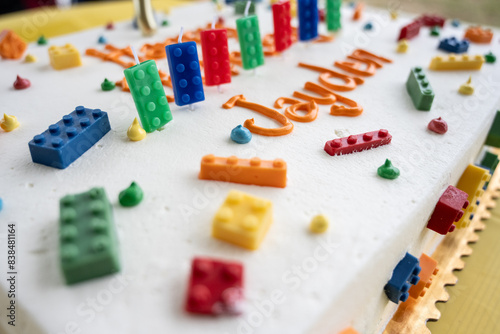 Birthday cake has white frosting and decorated with colorful building blocks as candles