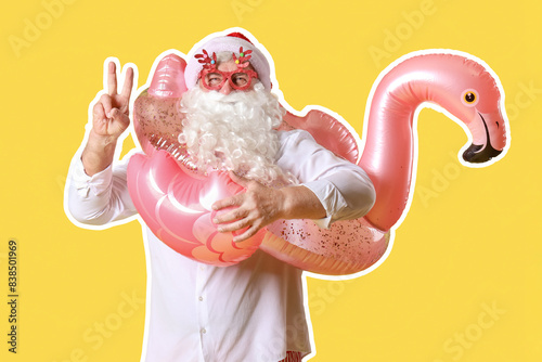 Santa Claus with swim ring showing victory gesture on yellow background. Christmas in July