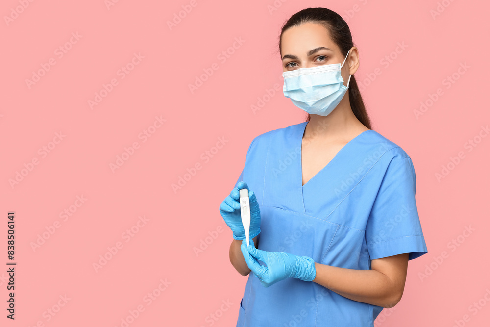 Portrait of female doctor in mask with digital thermometer on pink background Portrait of female doctor in mask with digital thermometer on pink background