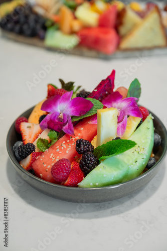 Bowl of colorful fruit salad with exotic fruit berries and melons decorated with purple orchids, Vertical  photo