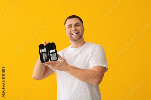 Handsome young happy diabetic man holding case with glucometer and lancet pens on yellow background