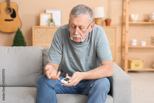 Senior man checking blood sugar level at home. Diabetes concept